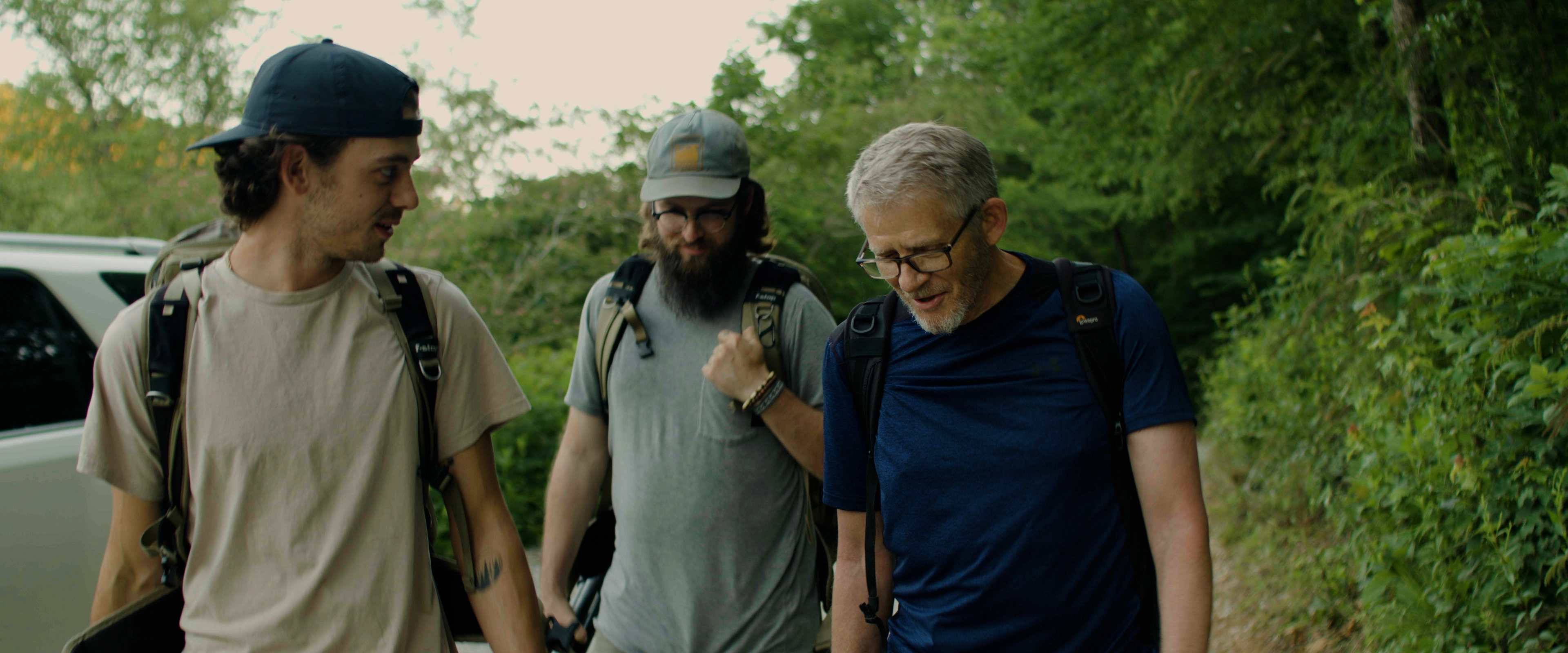 Three men with backpacks walking along a wooded trail